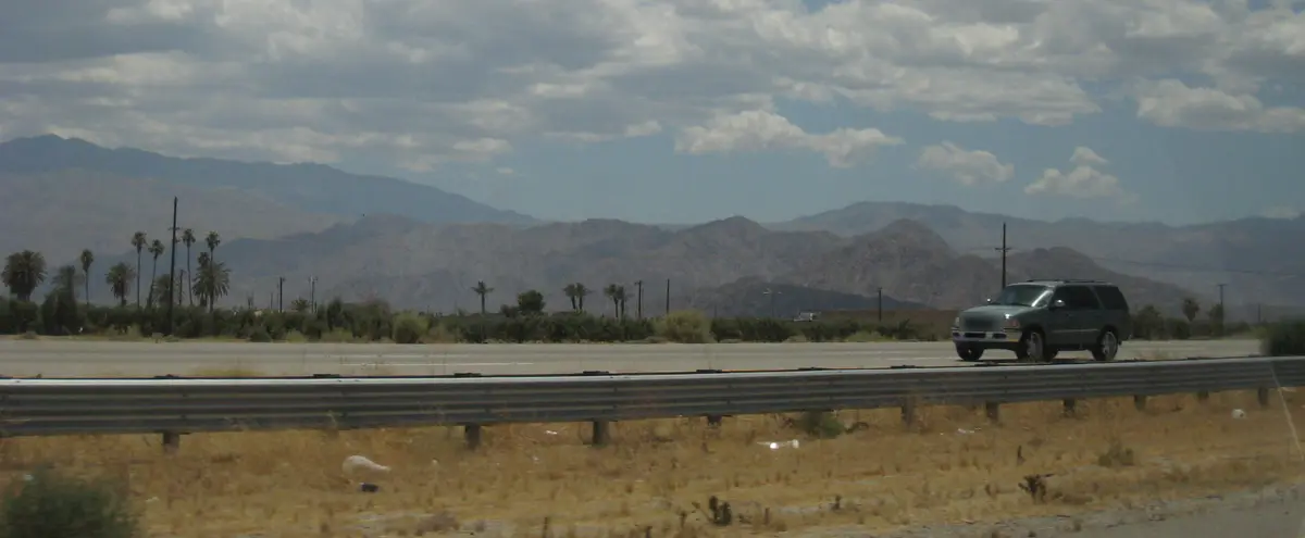 Interstate 10 near Indio with a guardrail and dry shoulder, palm trees and mountains behind