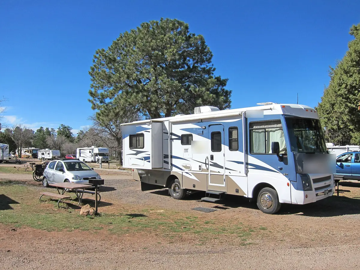 Class C motorhome with a slide-out parked at a campground with pine trees