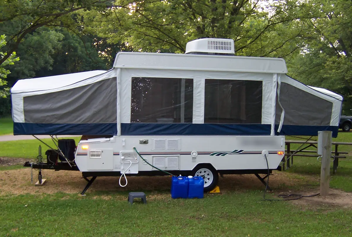 Pop-up camper at a campsite with its corner stabilizer jacks lowered and the tongue jack resting on a block
